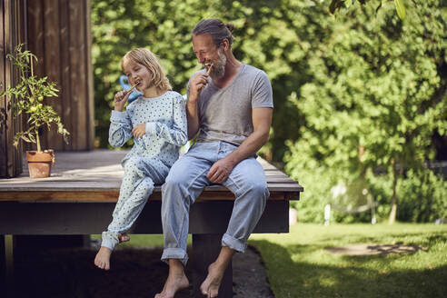 Father and daughter brushing teeth while sitting in yard - MCF01462