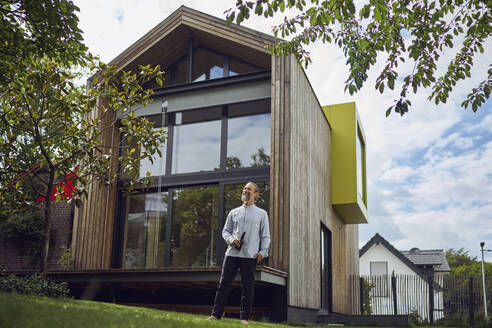 Mature man with beer bottle while standing outside modern tiny house - MCF01472