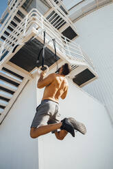 Sportler, der an einem Ring an einer Treppe im Freien hängend trainiert - MIMFF00206