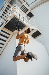 Sportsperson exercising while hanging on ring at staircase outdoors - MIMFF00206