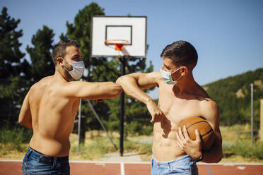 Sportler mit Gesichtsmaske grüßt mit Ellenbogenstoß auf Basketballplatz - MIMFF00217