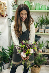 Frau lächelt, während sie einen Blumenstrauß im Blumenladen hält - MRRF00401
