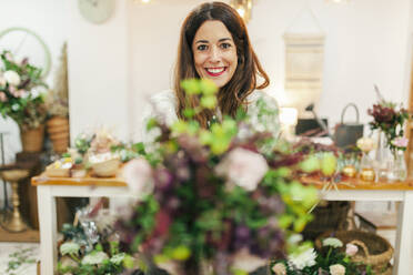 Smiling woman holding bouquet while standing at flower shop - MRRF00403