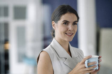 Businesswoman taking coffee break while standing at office - KNSF08426