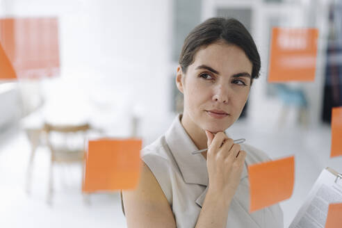 Thoughtful businesswoman standing with hand on chin at office - KNSF08435