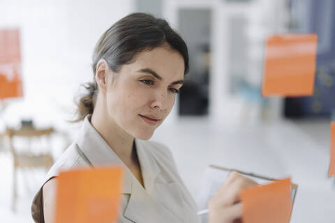 Young woman writing on sticky note while standing at office stock photo