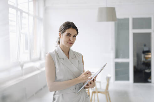 Businesswoman holding notepad while standing at office - KNSF08438