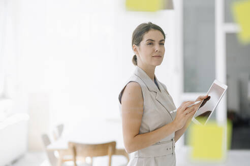 Confident businesswoman using digital tablet while standing at office - KNSF08446