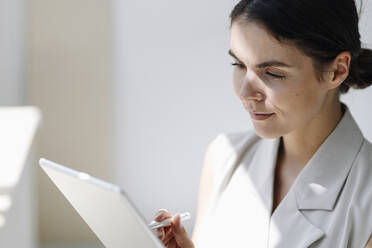 Businesswoman using digital tablet while standing at office - KNSF08447