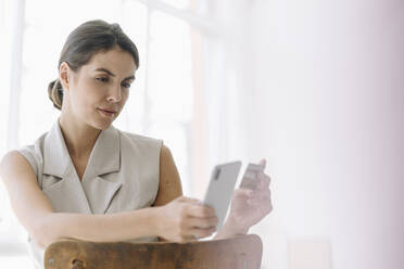Businesswoman holding credit card while using mobile phone at office - KNSF08460