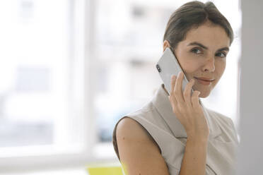 Beautiful businesswoman talking on mobile phone while standing at office - KNSF08463