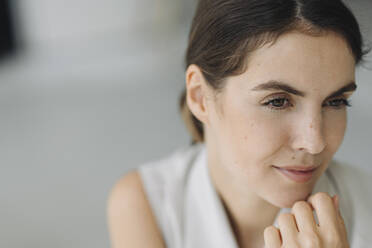 Thoughtful young woman with hand on chin sitting at office  - KNSF08478