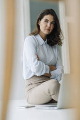 Businesswoman sitting on floor with laptop at office - KNSF08502