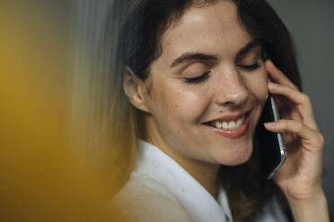 Junge Frau lächelt, während sie im Büro mit einem Mobiltelefon spricht - KNSF08510