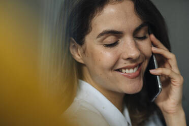 Young woman smiling while talking on mobile phone at office - KNSF08510