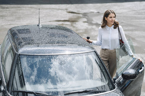 Young woman opening door of car while standing at parking lot - KNSF08516