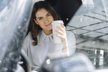 Smiling woman drinking coffee while sitting in car - KNSF08518