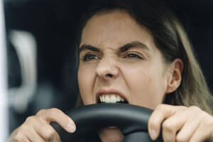 Nahaufnahme einer wütenden Frau, die ins Lenkrad beißt, während sie im Auto sitzt - KNSF08523