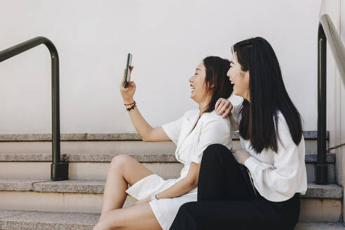 Coworkers taking selfie while sitting on staircase - MRRF00418