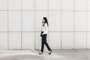 Businesswoman walking while talking on smart phone in city - MRRF00419