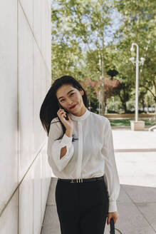 Smiling businesswoman standing in city while talking on smart phone - MRRF00422