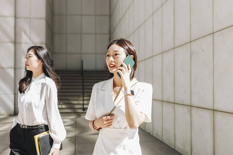 Coworker looking away while businesswoman talking on phone in city during sunny day stock photo