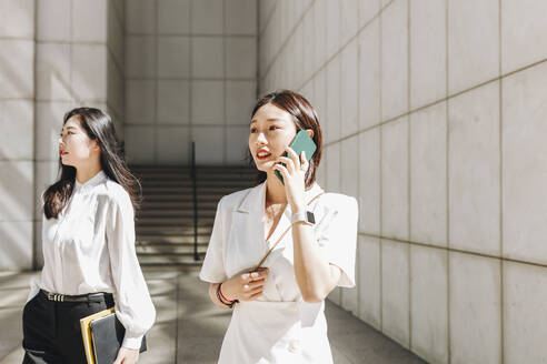 Coworker looking away while businesswoman talking on phone in city during sunny day - MRRF00423