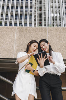 Female coworkers standing against financial district in city - MRRF00425