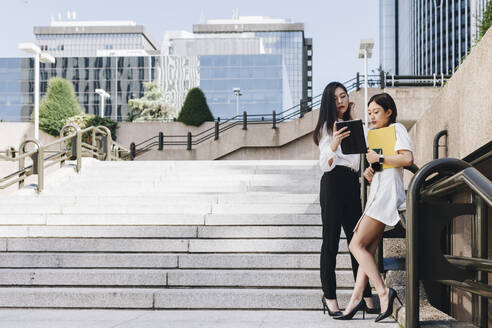 Female entrepreneurs standing on staircase against downtown district while using digital tablet - MRRF00427