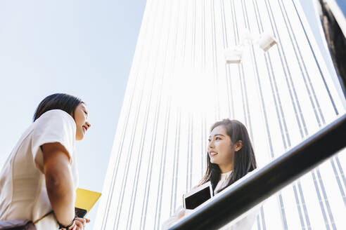 Female coworkers talking with each other on sunny day - MRRF00428