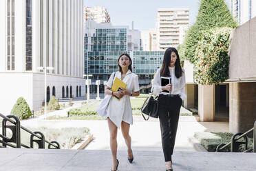 Female colleague walking together against downtown district in city - MRRF00429