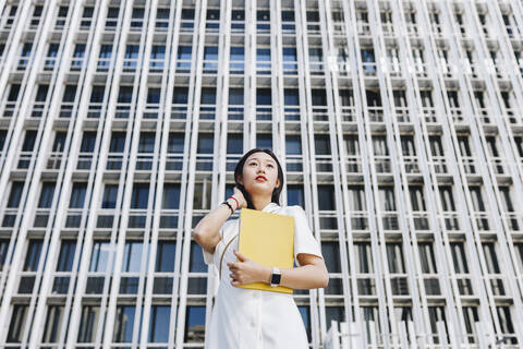 Female entrepreneur holding book while standing against financial district in city stock photo