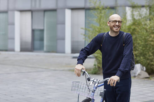 Lächelnder Mann mit Fahrrad auf der Straße stehend - MCF01485