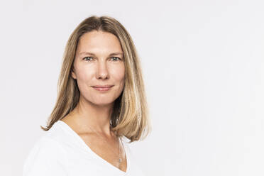 Close-up of smiling mature woman with blond hair against white background - SDAHF00970