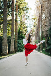 Junge Frau springt beim Tanzen auf der Straße zwischen Bäumen im Park - DCRF00835