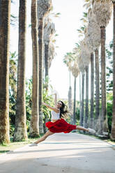 Balletttänzerin springt auf der Straße gegen Bäume im Park - DCRF00838