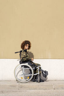 Female military officer sitting on wheelchair against wall - OCMF01670