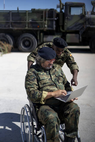 Ein behinderter Militäroffizier arbeitet an einem Laptop mit einem Kollegen an einem sonnigen Tag, lizenzfreies Stockfoto