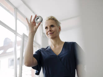 Businesswoman looking through object while standing in loft office - KNSF08547