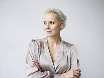 Thoughtful businesswoman with arms crossed standing against white wall in office - KNSF08554