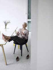 Lächelnde Geschäftsfrau mit hochgelegten Füßen, die sich auf einem Stuhl im Loftbüro entspannt - KNSF08562