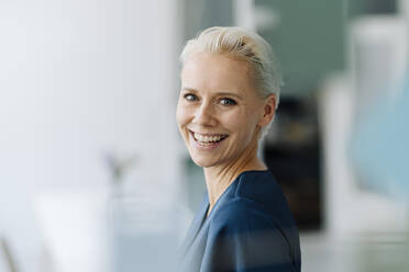 Close-up of cheerful businesswoman with short hair in office - KNSF08576