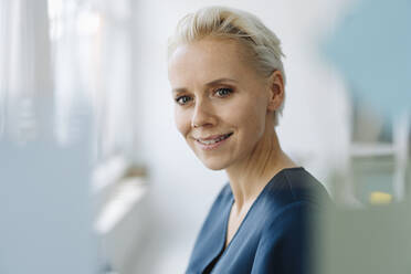 Close-up of smiling female entrepreneur seen through window in office - KNSF08583