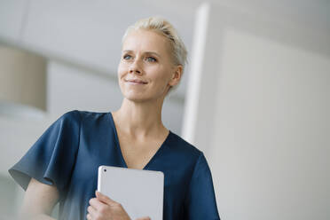 Nahaufnahme einer nachdenklichen Unternehmerin, die ein digitales Tablet in einem Loft-Büro hält - KNSF08588