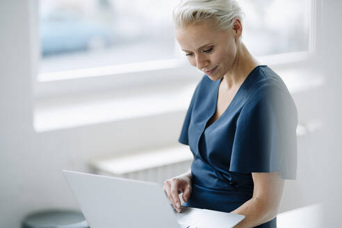 Businesswoman using laptop while sitting in loft office - KNSF08594