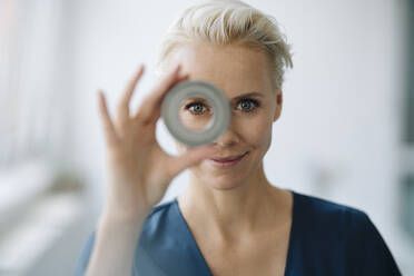 Close-up of smiling businesswoman looking through object in office - KNSF08596