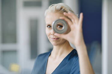 Close-up of confident businesswoman looking through object in office - KNSF08598