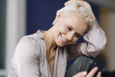 Close-up of smiling businesswoman using mobile phone while sitting in office - KNSF08638