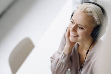 Nahaufnahme einer lächelnden Frau, die im Büro über Kopfhörer Musik hört - KNSF08652