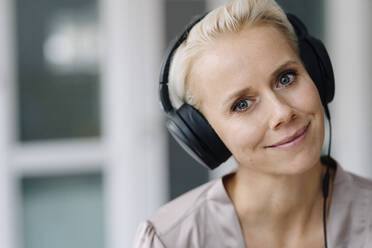 Close-up of smiling businesswoman listening music over headphones in office - KNSF08653